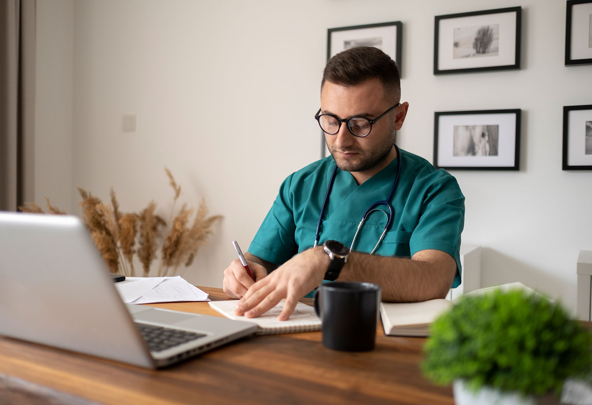 Porträt von lächelndem, männlichem Arzt trägt grünen Mantel mit Stethoskop sitzt hinter Schreibtisch im Büro