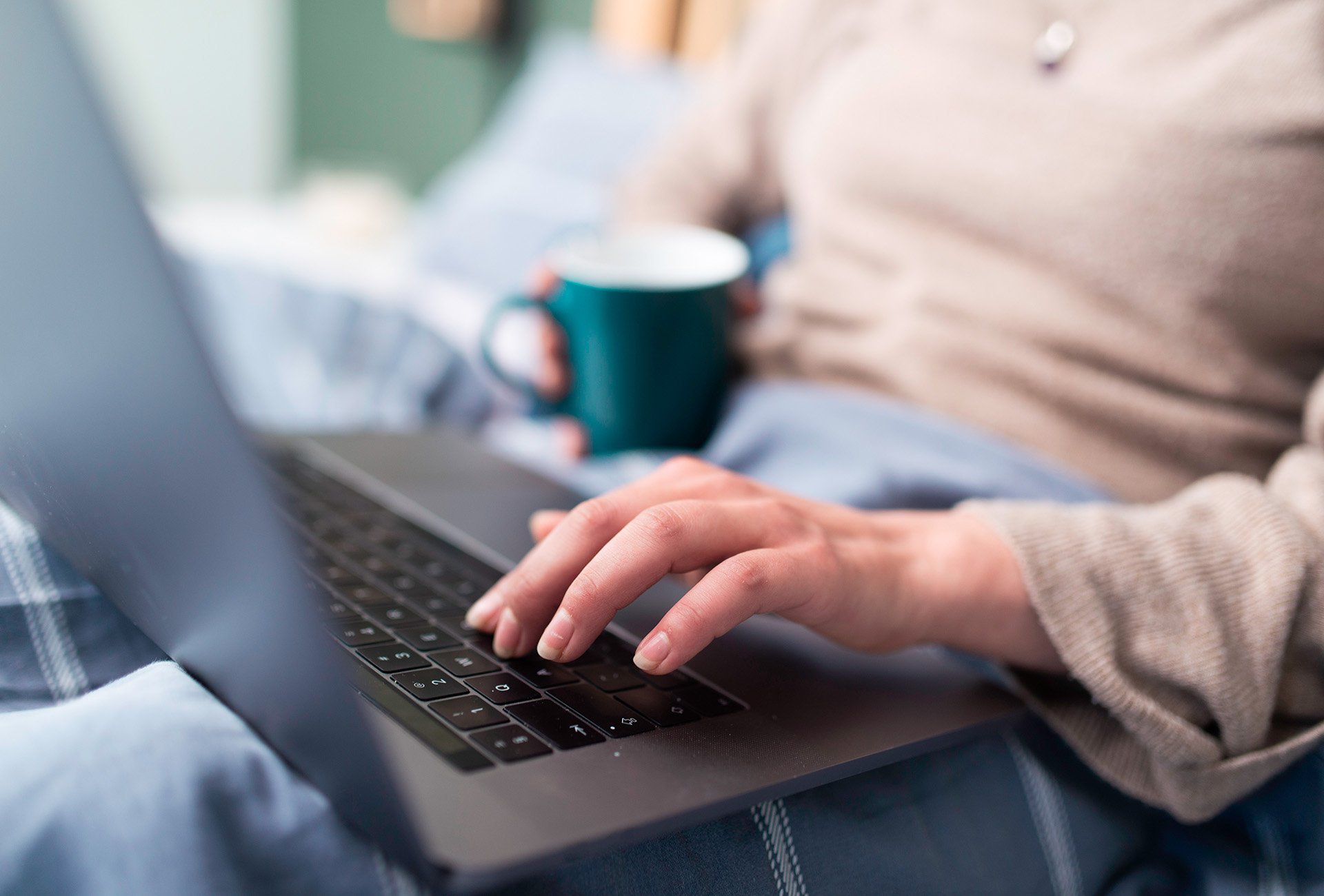Frau mit Laptop und Kaffeetasse gemütlich auf der Couch