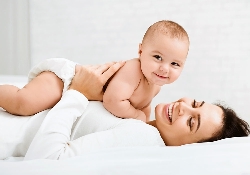 Mama spielt mit Baby in Windeln, beide strahlen