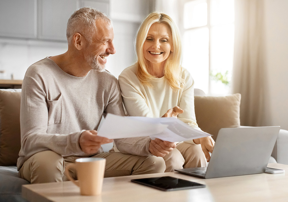 Lächelndes älteres Paar, das Papiere hält und etwas berechnet